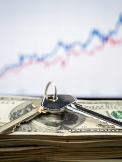 House key on dollar bills with rising interest rate graph