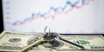 House key on dollar bills with rising interest rate graph